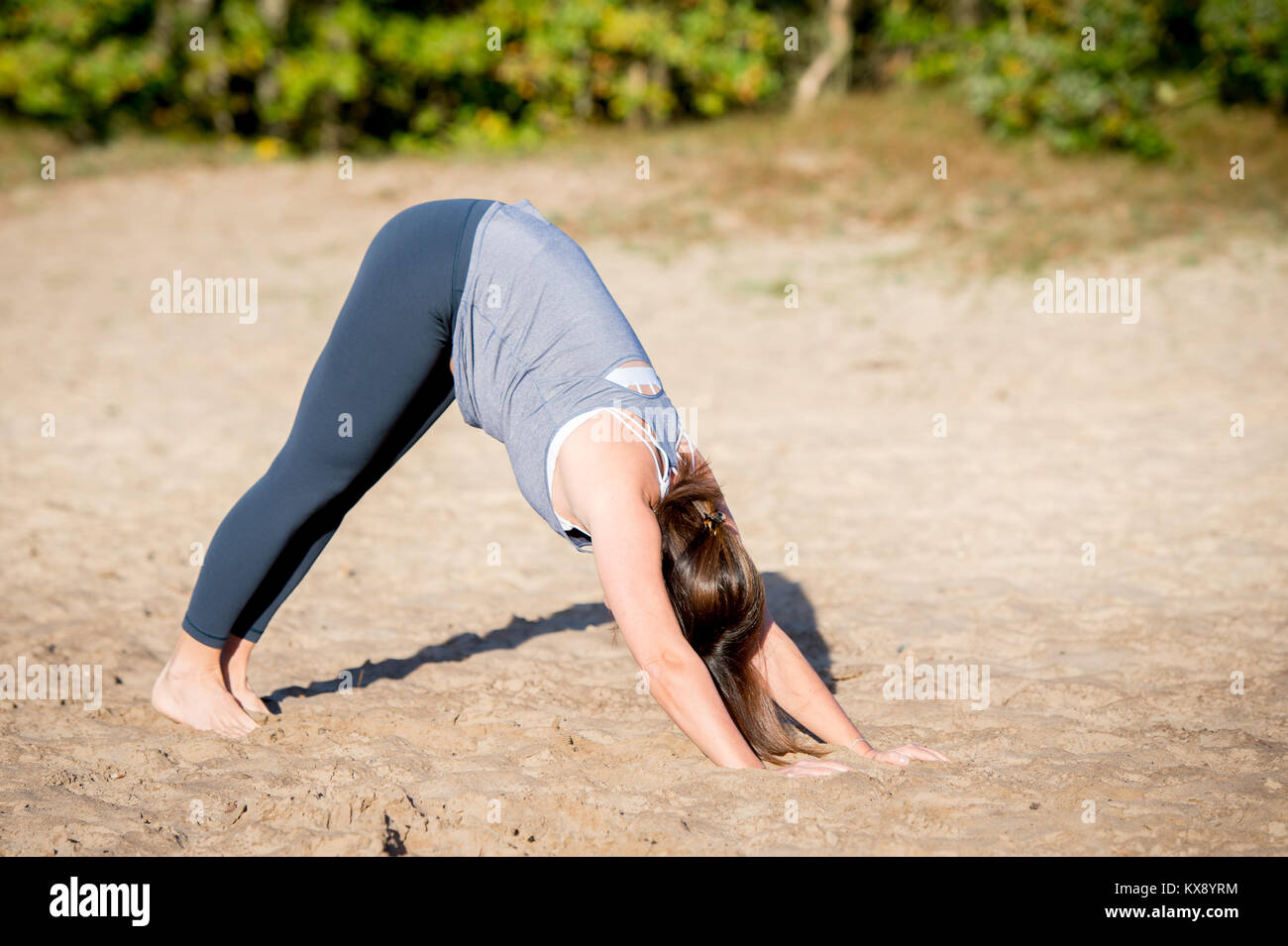 Woman practicing yoga in the sand - Downward Facing Dog - Autumn day Stock Photo