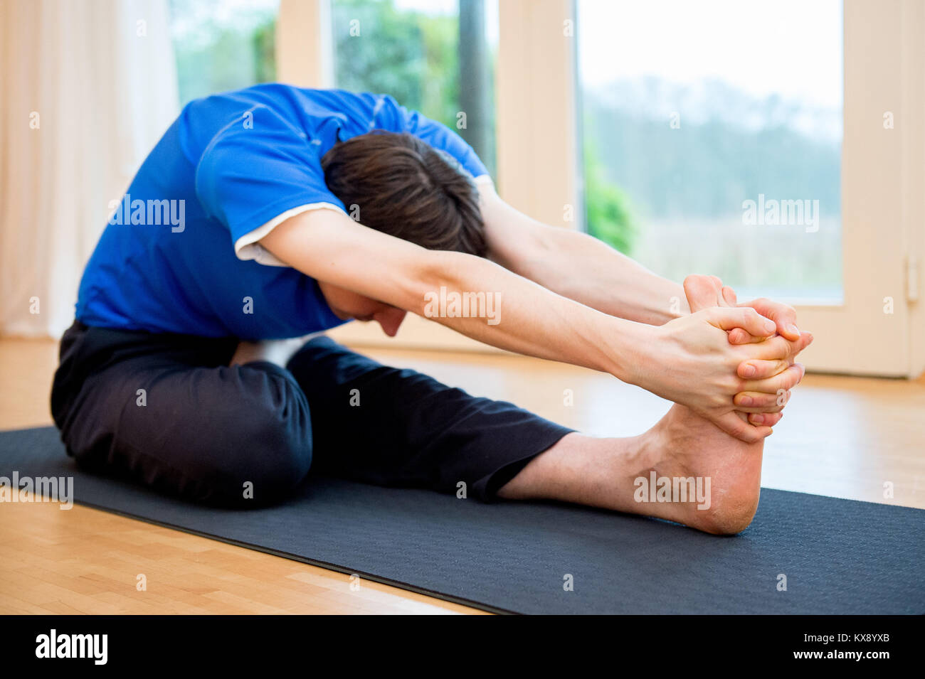 Man practicing yoga indoors in a retreat space doing Head-to-Knee Forward Bend Pose - Janu Sirsasana Stock Photo