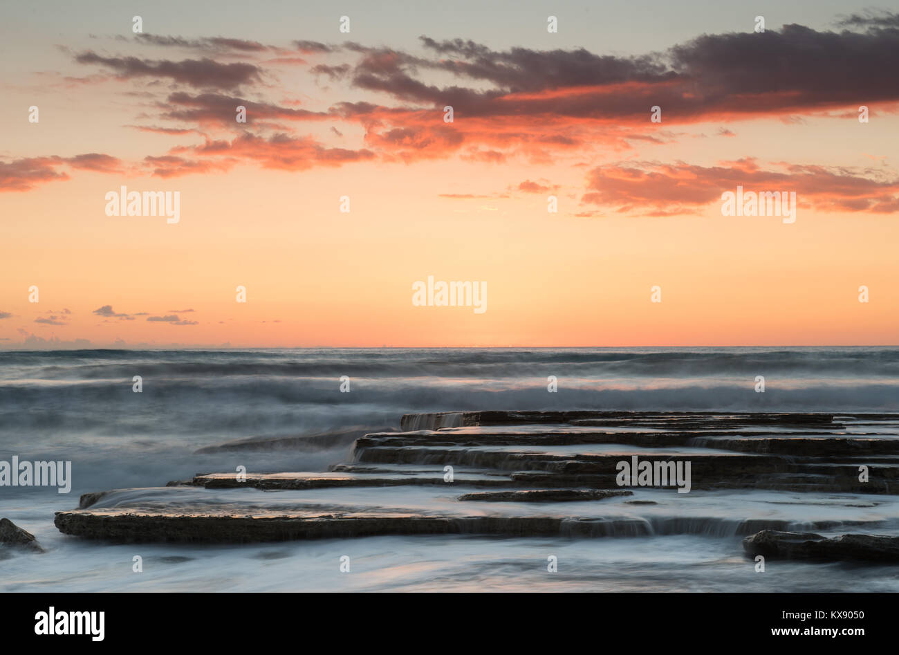 Idyllic beautiful dramatic orange sunset over a rocky waving coast Stock Photo