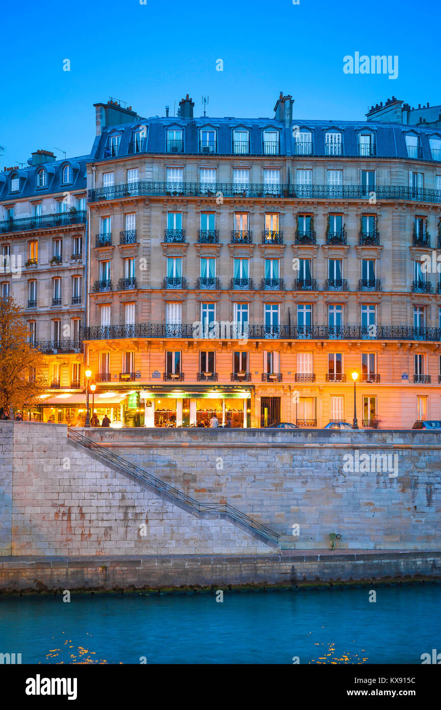 Paris night quai, as night falls the lights of a cafe illuminate the base of a typical apartment building on the Ile St-Louis in central Paris, France Stock Photo