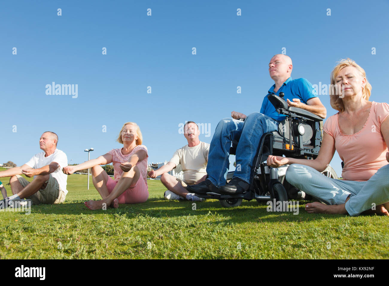 Disabled man with group of people practicing yoga outside. Stock Photo