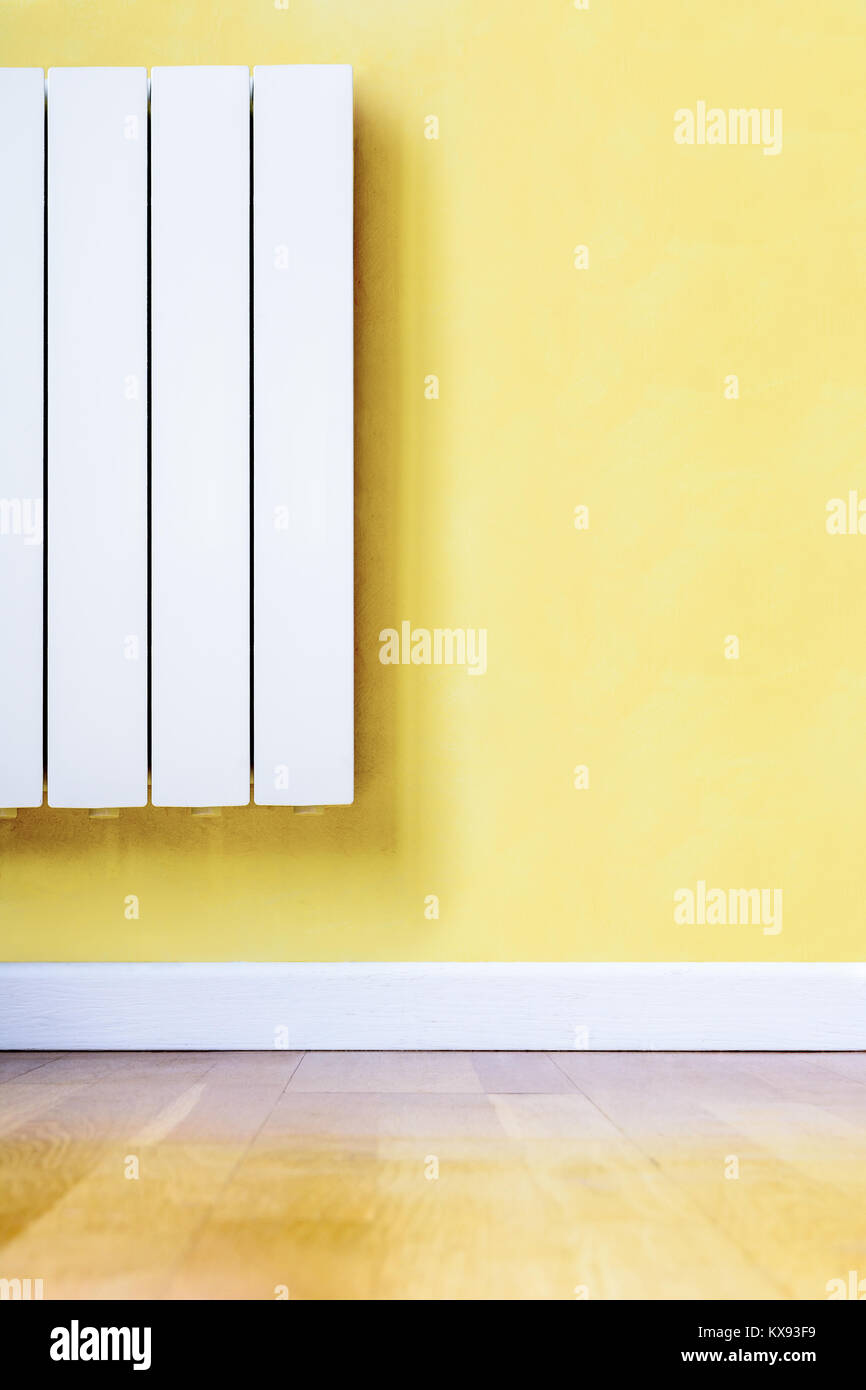 Modern white electric heater with electronic thermostat fitted in a room with yellow wall, wooden floor and white baseboard. Stock Photo