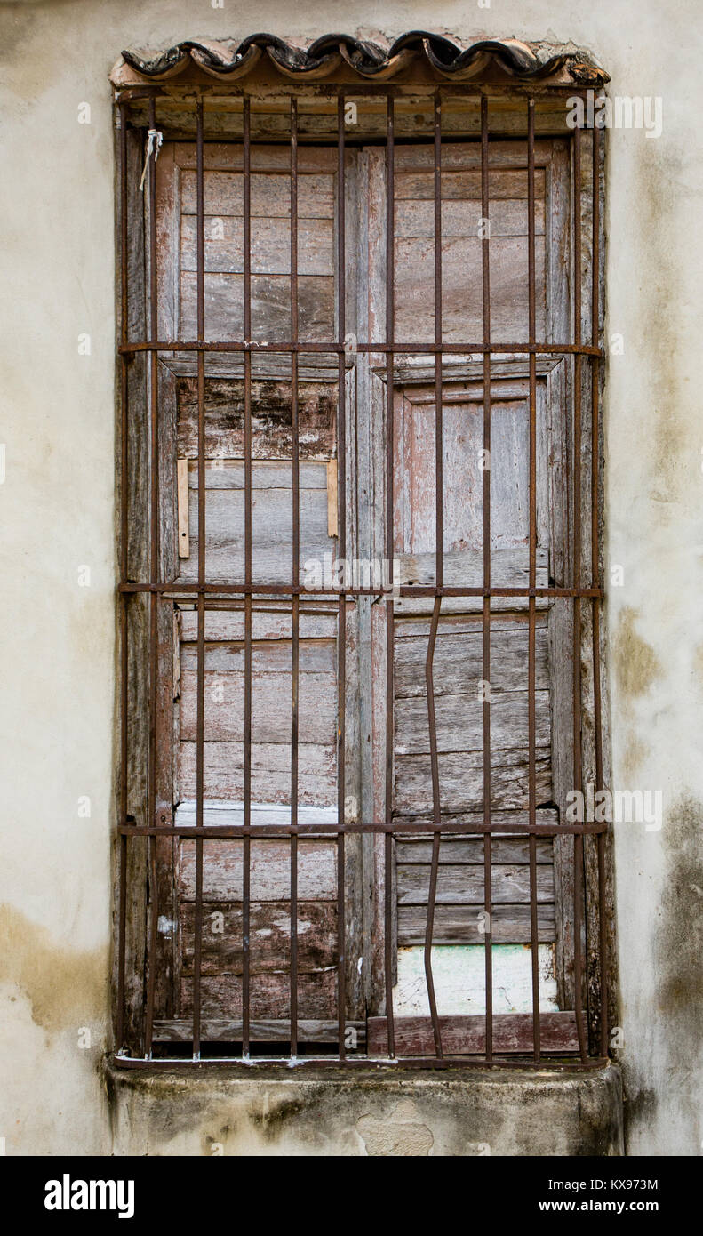Old unpainted white shutters in window behind rusted iron bars on