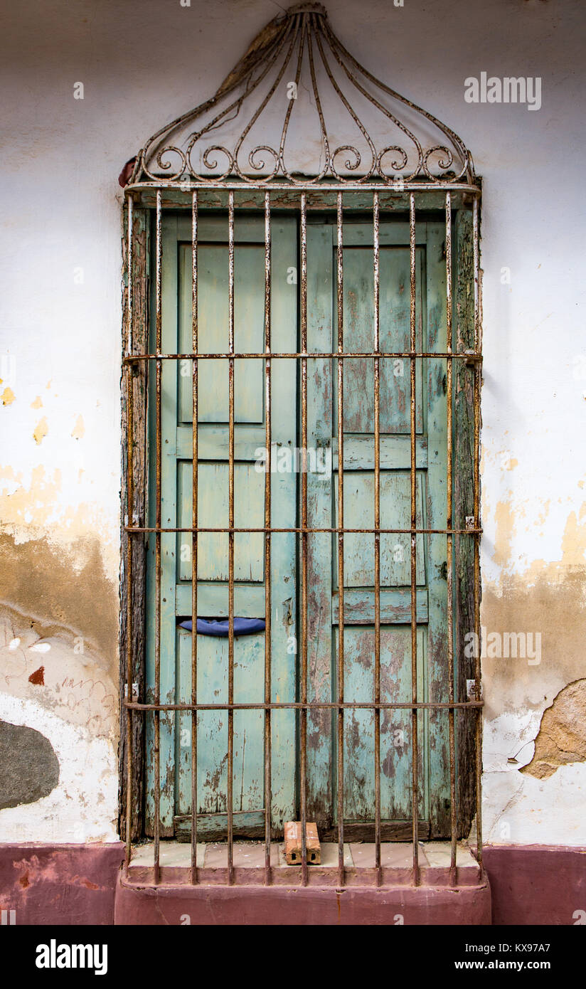 Faded green door with padlock behind metal grate on stained white wall