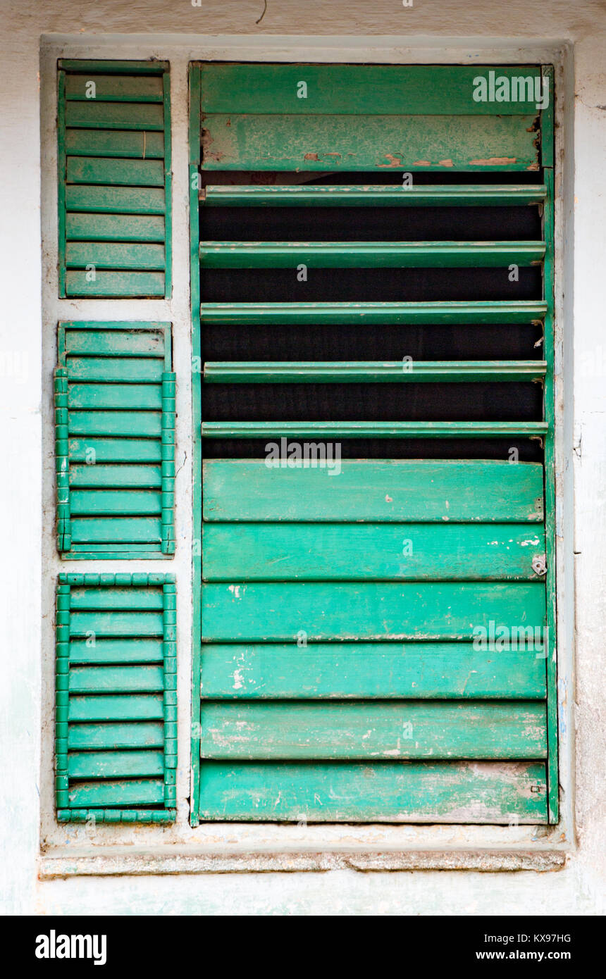 Partially open chipped green shutters in window on white wall in