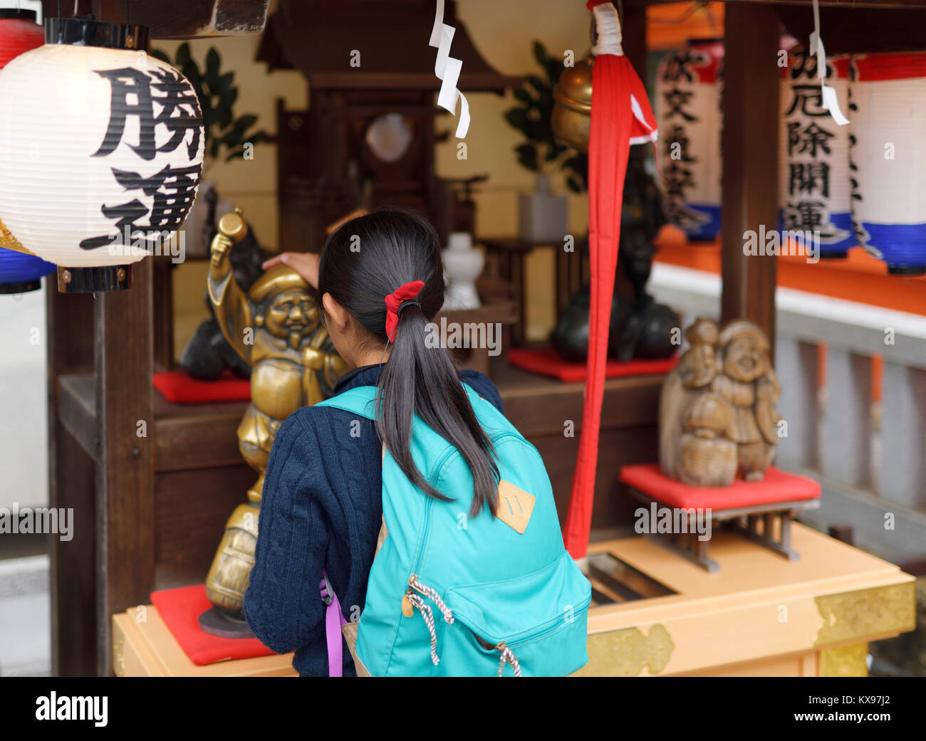 A girl patting Daikoku, one of the Seven Lucky Gods, a deity bringing wealth, at Jishu Jinja Shinto shrine of Kiyomizu-dera Buddhist temple in Higashi Stock Photo