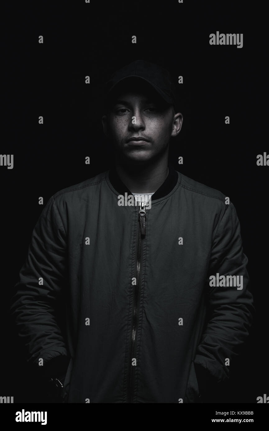 teen boy posing with black cap and bomber jacket in front of black background Stock Photo