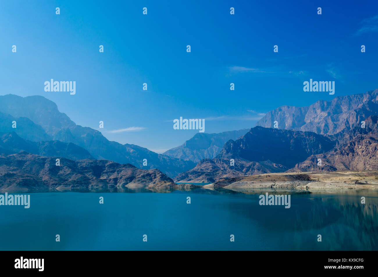 Waterscape with calm waters with reflection, mountains and blue sky on a bright sunny day, in Muscat, Oman. Stock Photo