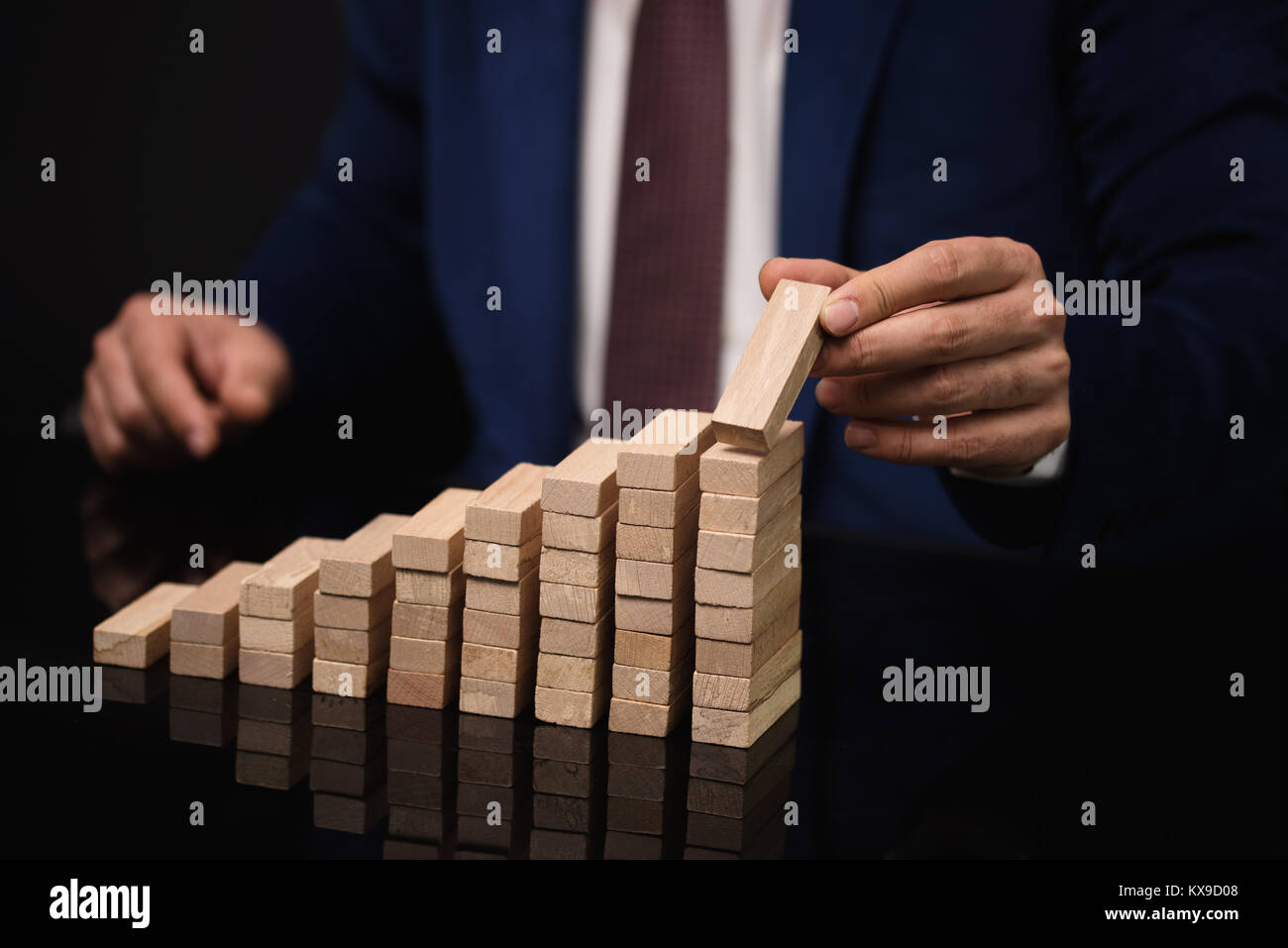 Businessman building a increasing graph or ladder of success on black table. Stock Photo