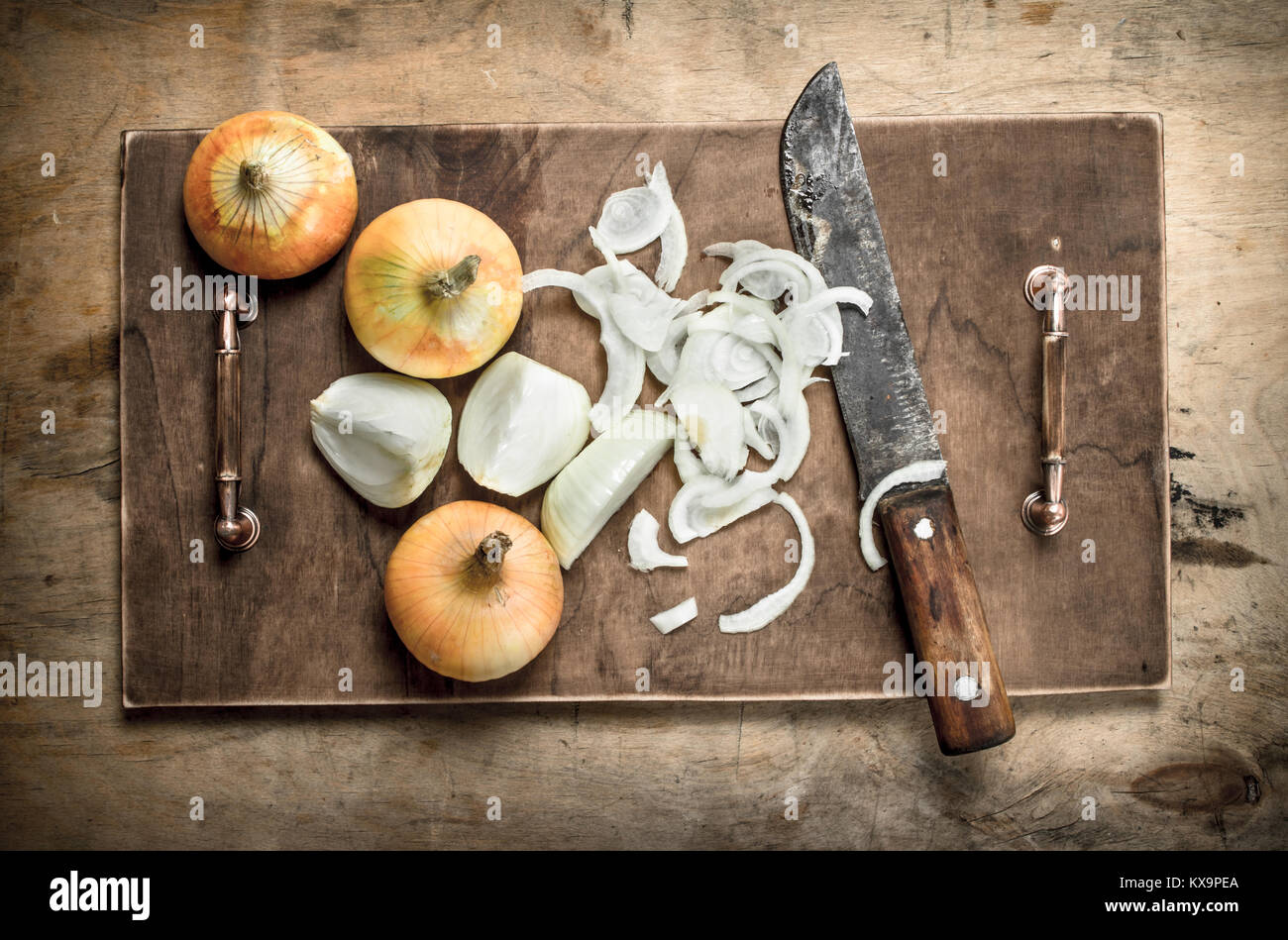 Slicing fresh onion on a cutting board with an old knife. On a wooden ...