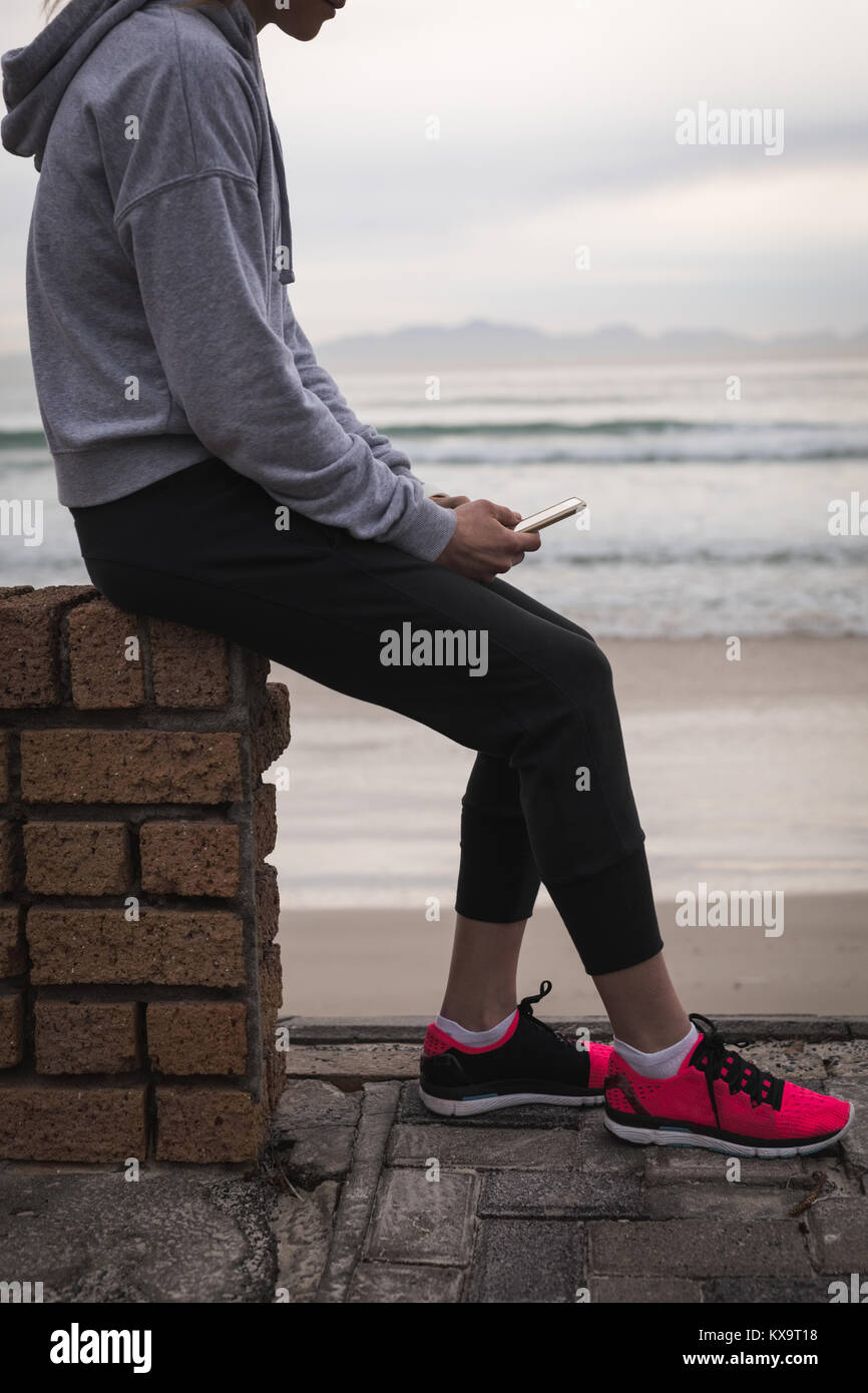 Young woman sitting on a wall at beach Stock Photo - Alamy
