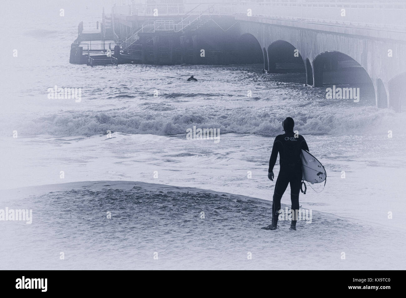 surfer standing on the beach near Bournemouth pier looking out to sea