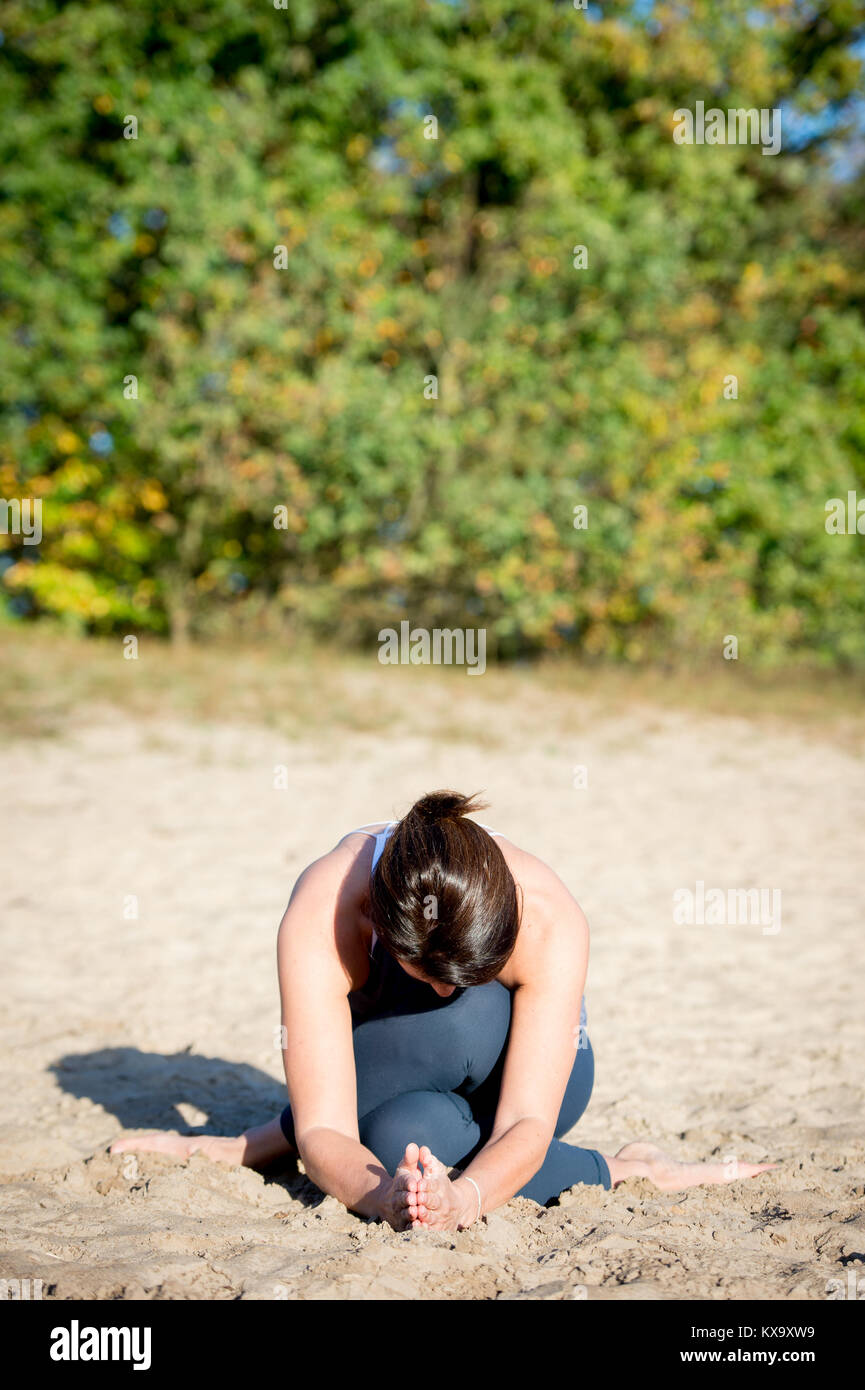 Woman practicing yoga in the sand - Shoelace pose - Autumn day Stock Photo