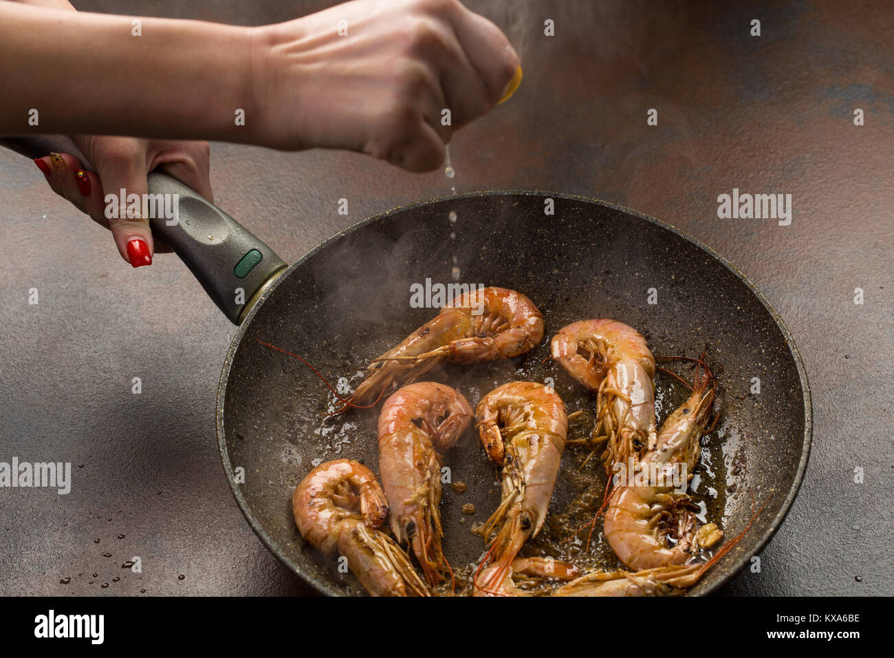 A hand squeezing lemon juice on roasted, grilled large tiger shrimps or langostonos over grey background. process of preparation Stock Photo