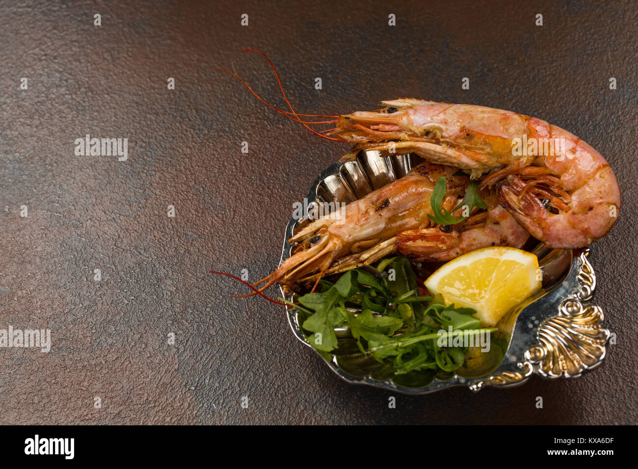 Two Fried Tiger Prawns or langostinos with greens and Lemon on ancient plate over dark background. Close-up view. Space for text Stock Photo