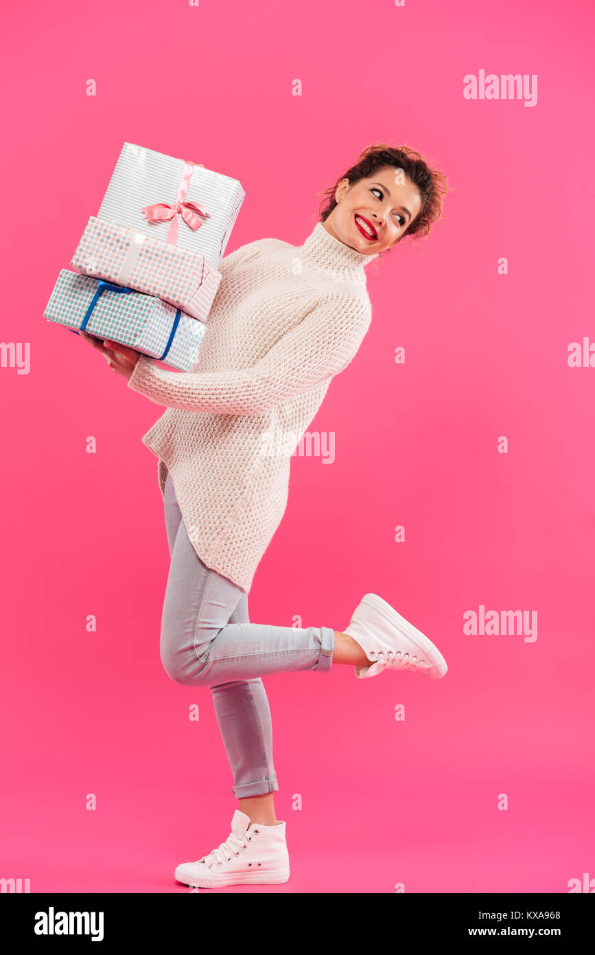 Full length portrait of a smiling pretty girl holding stack of gift ...
