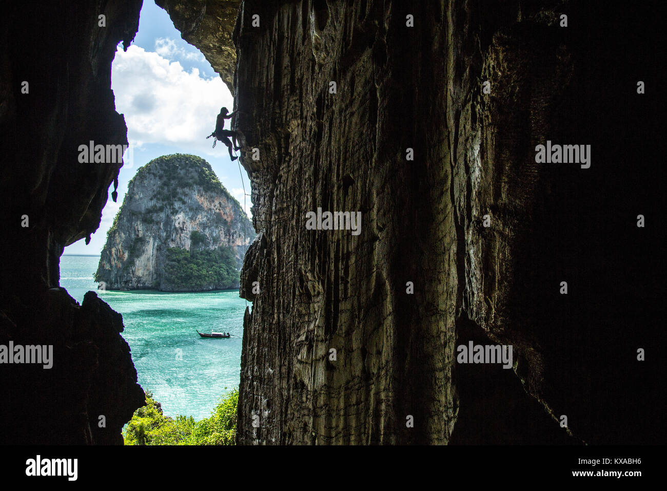Side view silhouette of man rock climbing in beautiful natural scenery on edge of cave, Phra Nang Beach, Krabi, Thailand Stock Photo