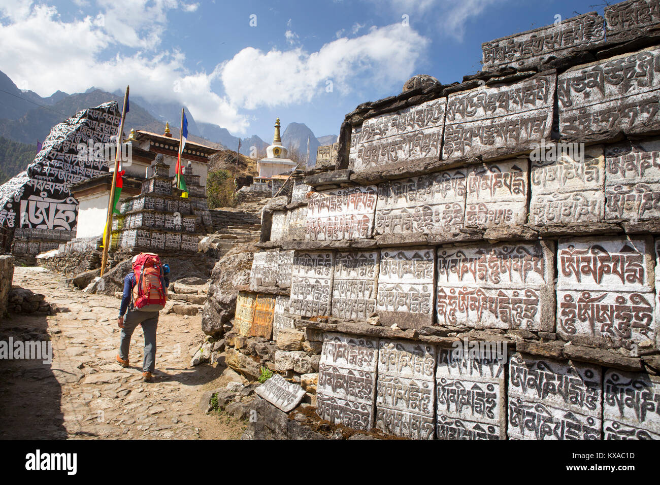 A trekker is walking past a big wall of Mani stones, with Buddhist prayer inscriptions. Stock Photo
