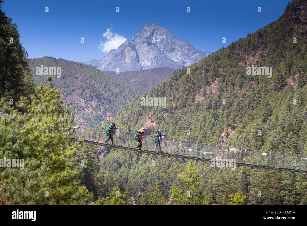 Three porters are crossing a Nepalese suspension bridge over a deep gorge on the way to Namche Bazar. Stock Photo