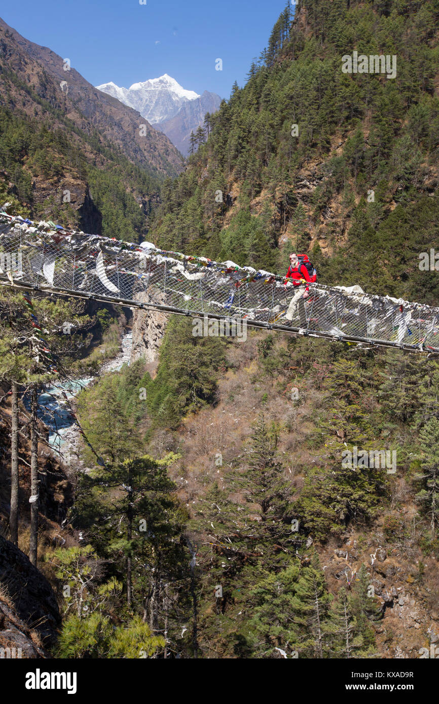 A solo male hiker is crossing a Nepalese suspension bridge over a deep gorge on the way to Namche Bazar. Stock Photo