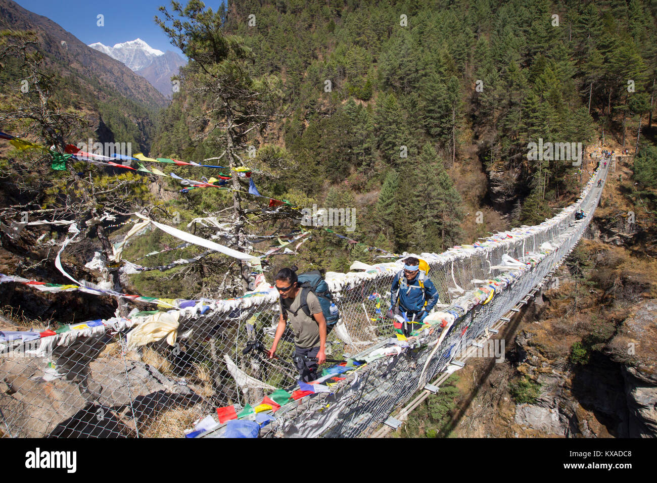 Two hikers are crossing a Nepalese suspension bridge over a deep gorge on the way to Namche Bazar. Stock Photo