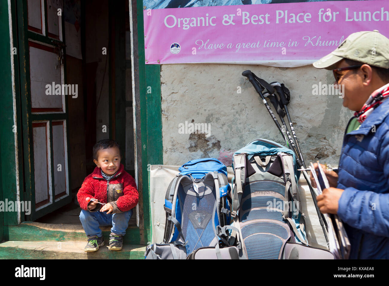 A trekker is talking to a young Nepalese boy at a tea house where hikers can rest and eat. Stock Photo