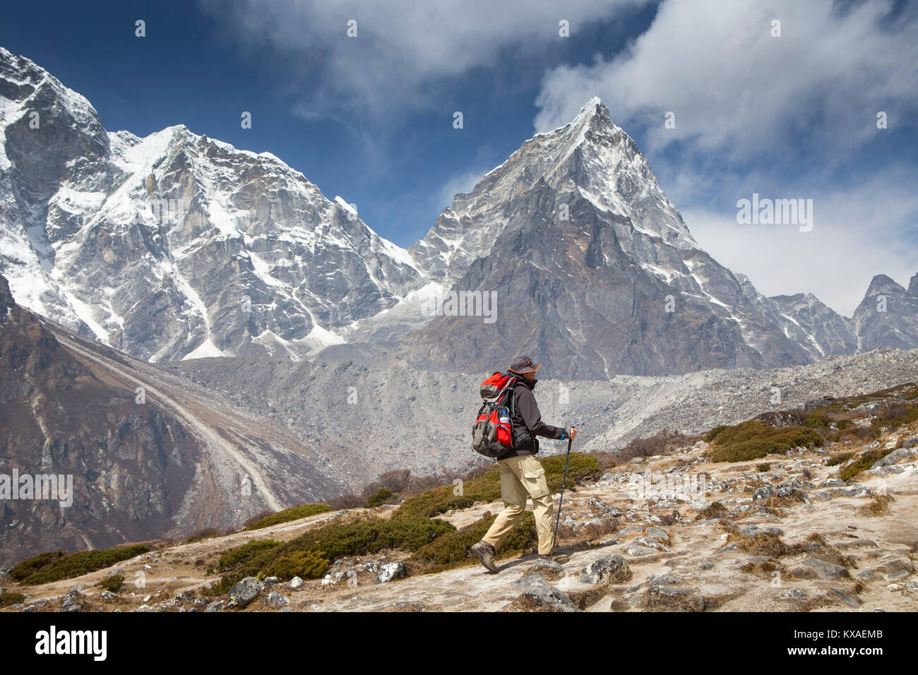 A hiker on his way to Everest Base Camp with the majestic Cholatse mountain in the background.  In the evenings you will be rewarded with delicious Nepalese cuisine around the dining-room fire while sipping Sherpa tea and conversing with other like-minded travelers. Stock Photo