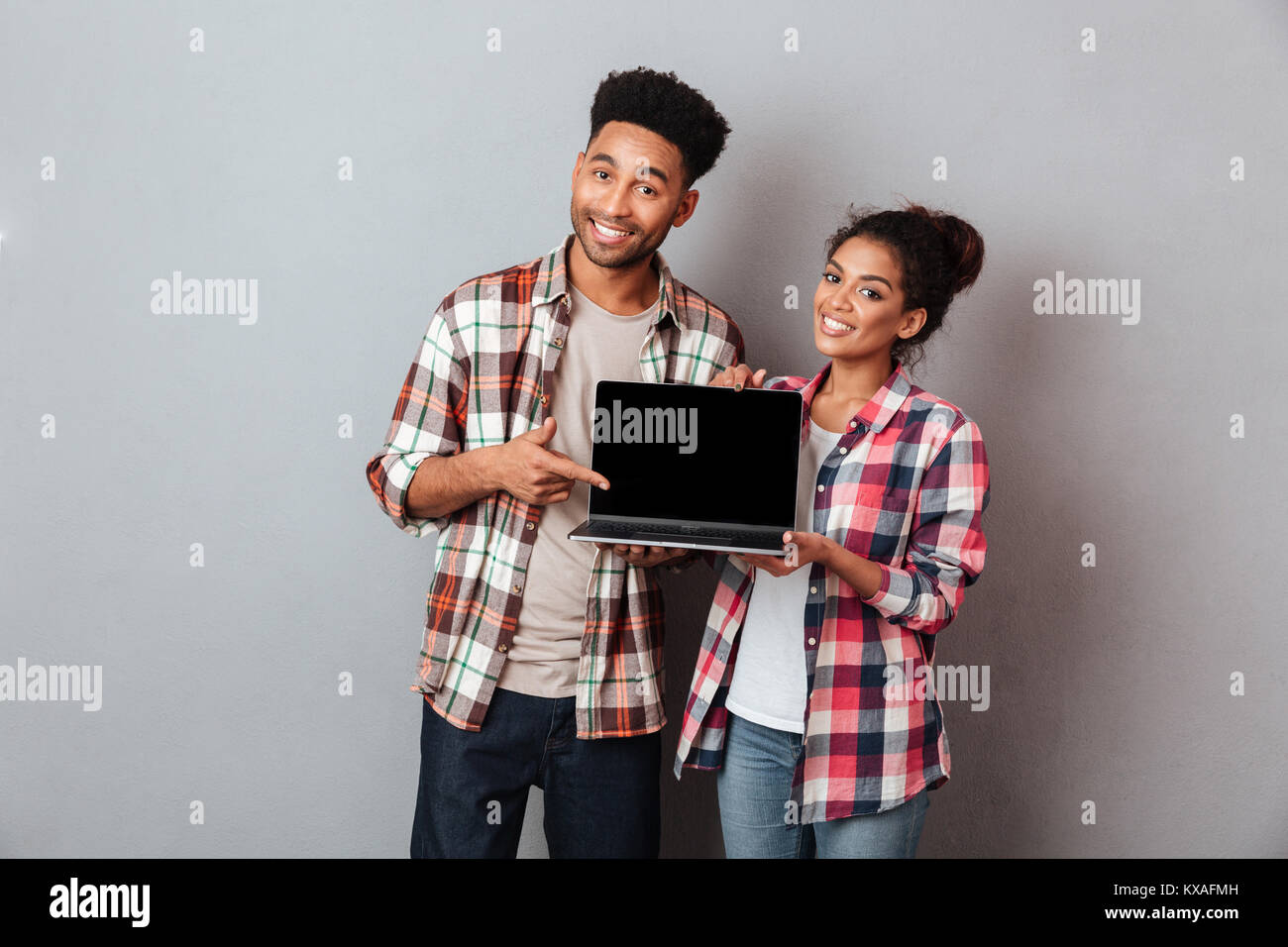 Portrait of a smiling young african couple showing blank screen laptop ...