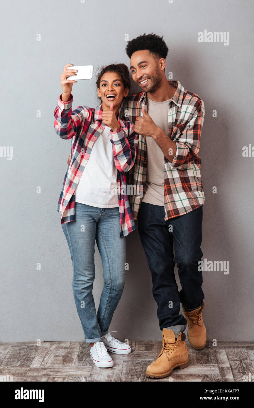 Full length portrait of a cheerful young african couple showing thumbs ...