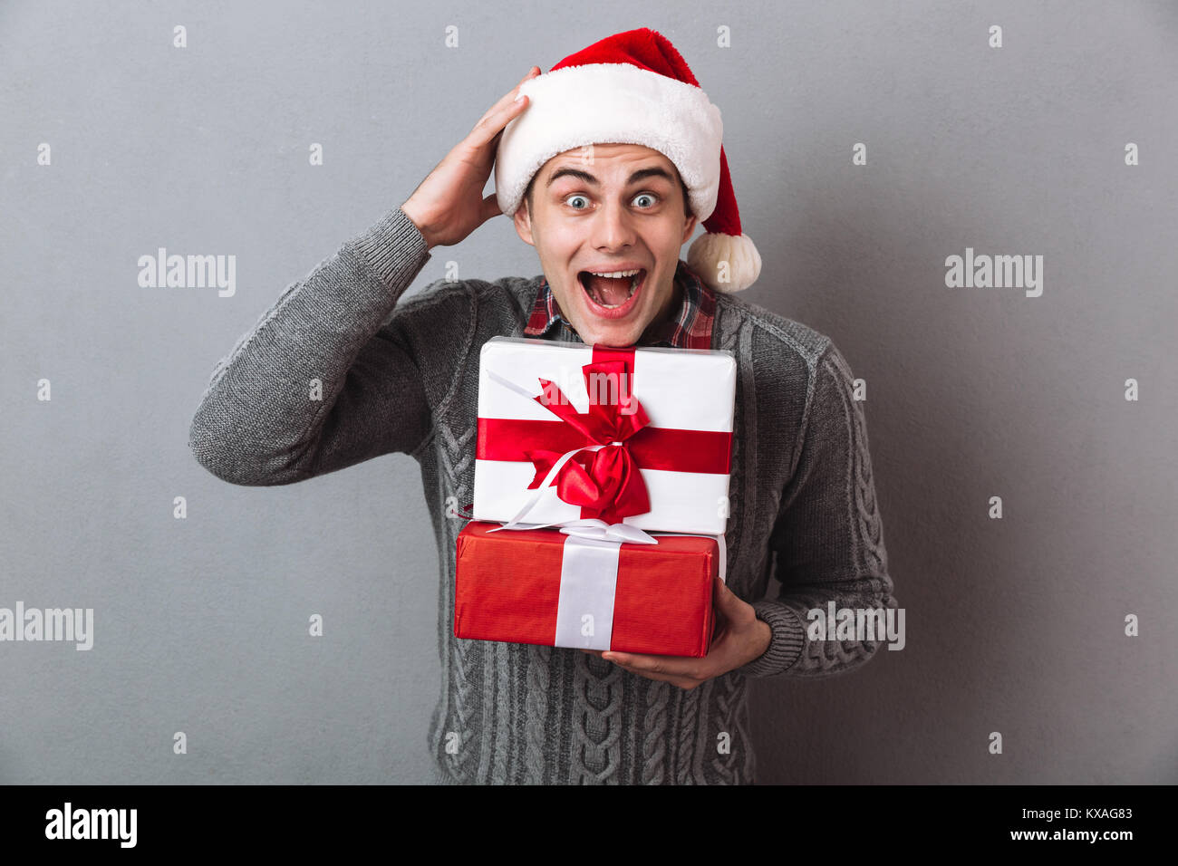 Man Raging Out Gift Shocked man in sweater and christmas hat holding gifts and looking at ...