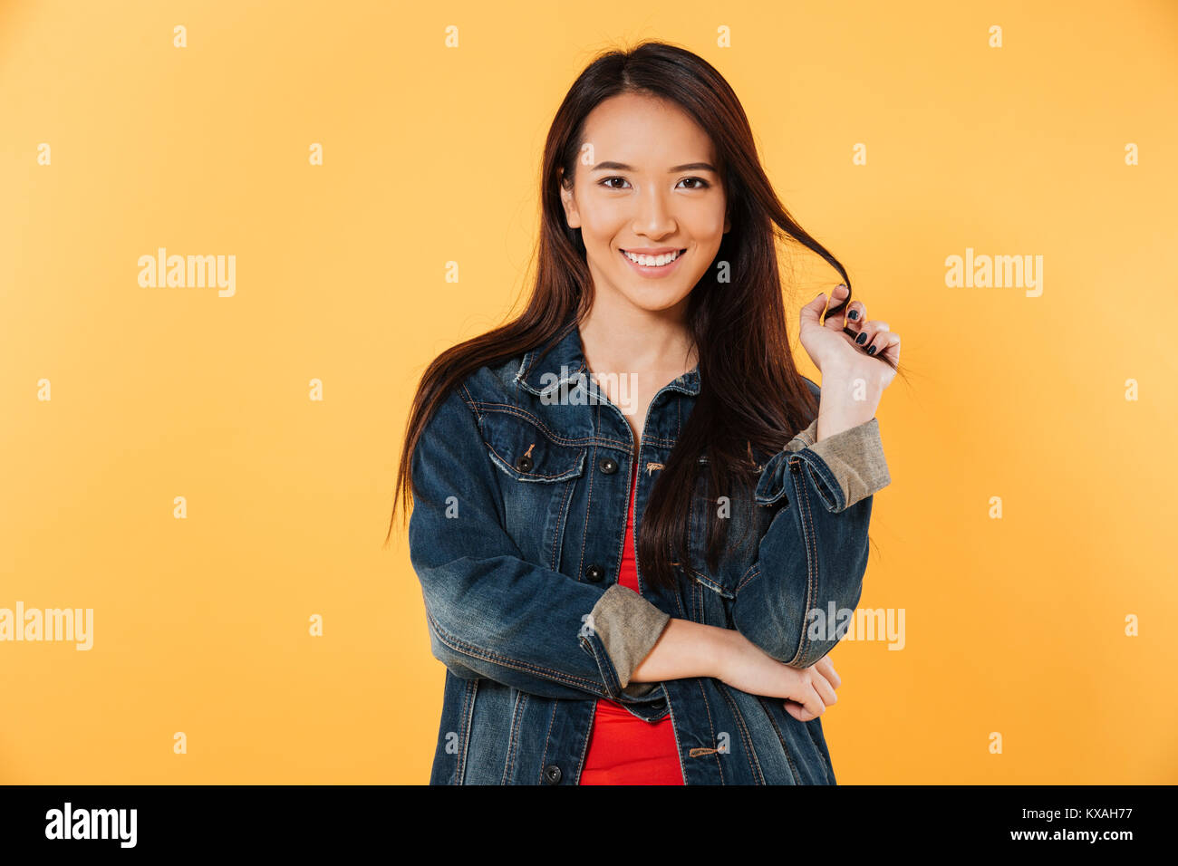 Smiling asian woman in denim jacket holding her hair and looking at the ...