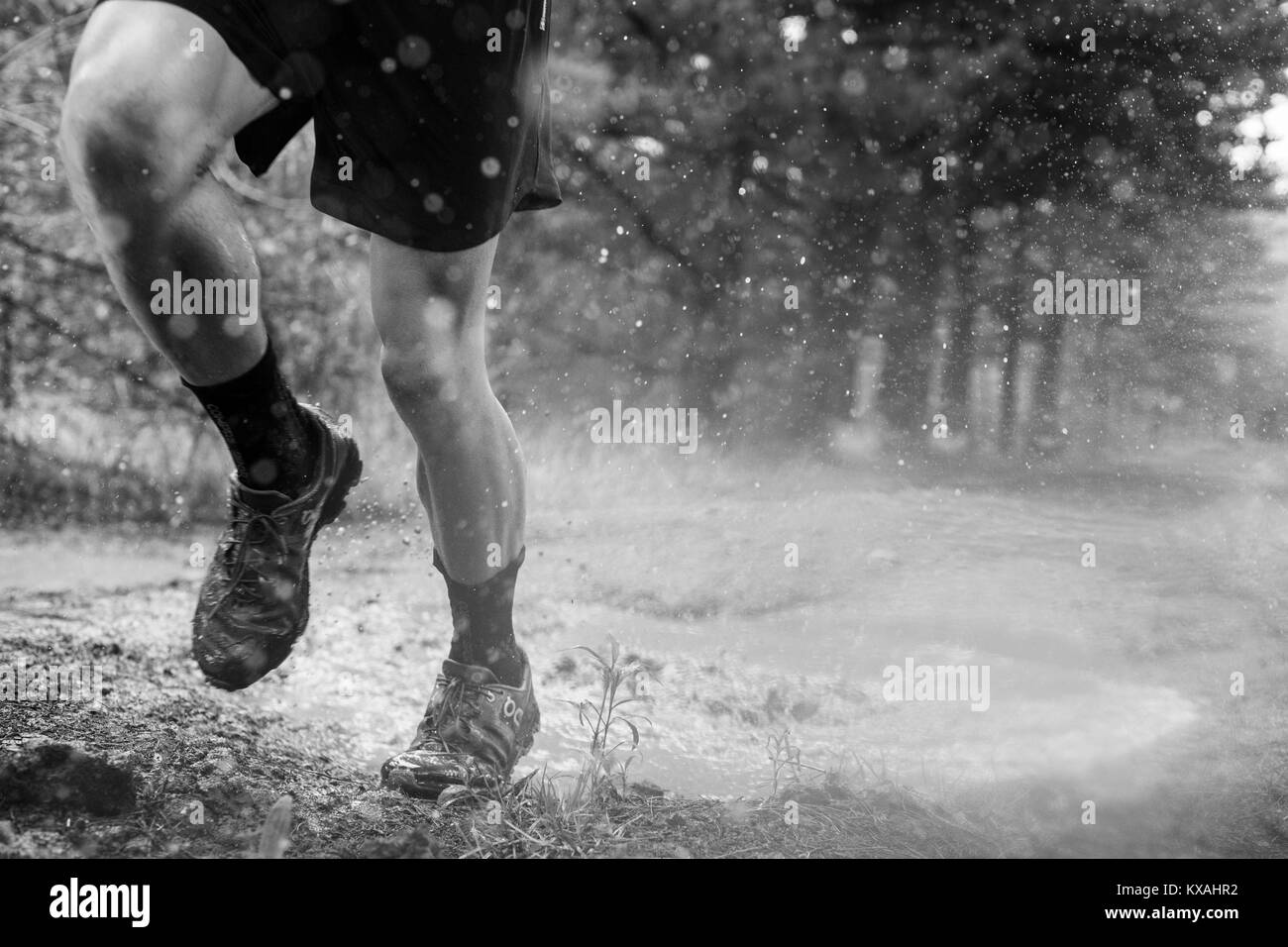 Low section of male runner splashing though puddle in Rancho Santa Elena, Hidalgo, Mexico Stock Photo