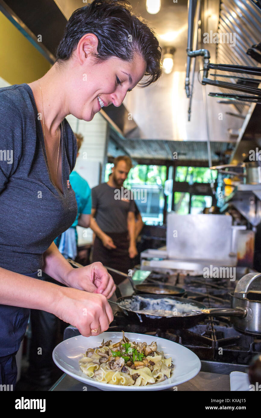 Female chef smiling while preparing beef stroganoff in restaurant kitchen, Portland, Oregon, USA Stock Photo