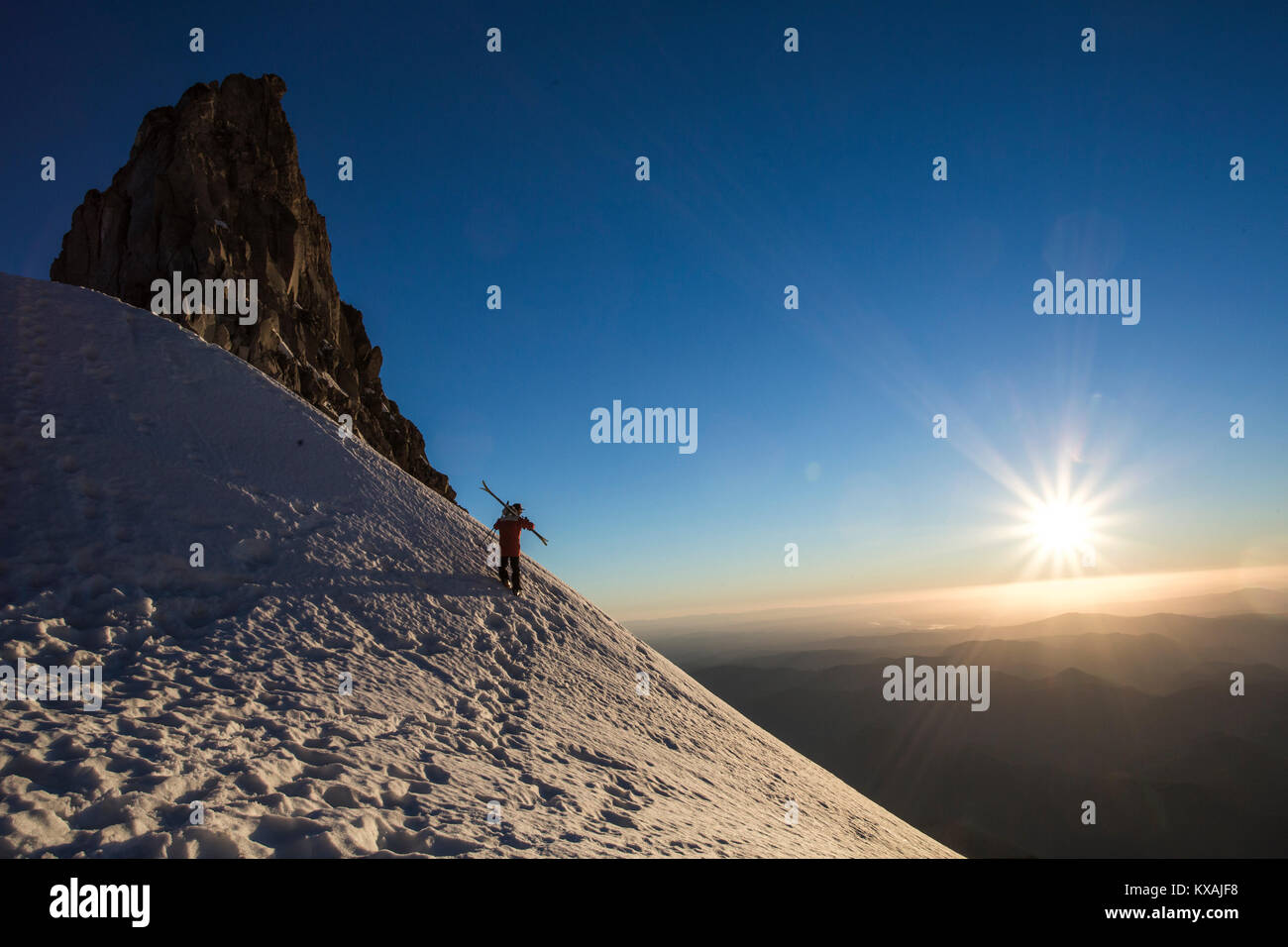 Skier carrying skis on snowy mountain with Sun setting in background, Mount Hood, Oregon, USA Stock Photo