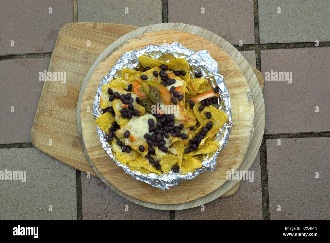 Mexican Nachos or Latin American - Close up of Black beans jalapeno pepper on corn tortilla chips with melted cheese on wooden platter. Stock Photo
