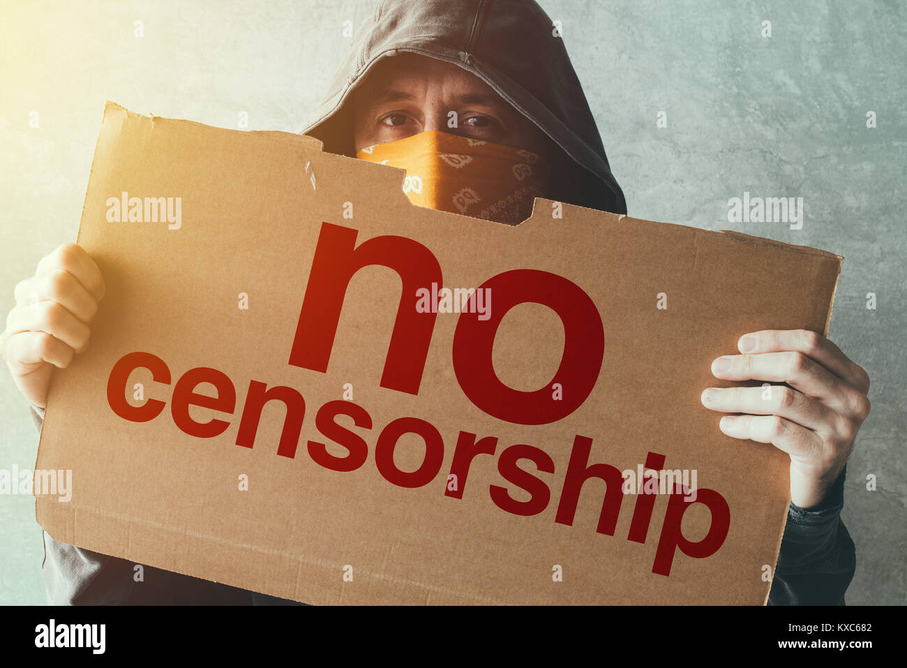 Hooded activist protestor holding No Censorship protest sign. Man with hoodie and scarf over face taking part in activism and fighting for the cause. Stock Photo