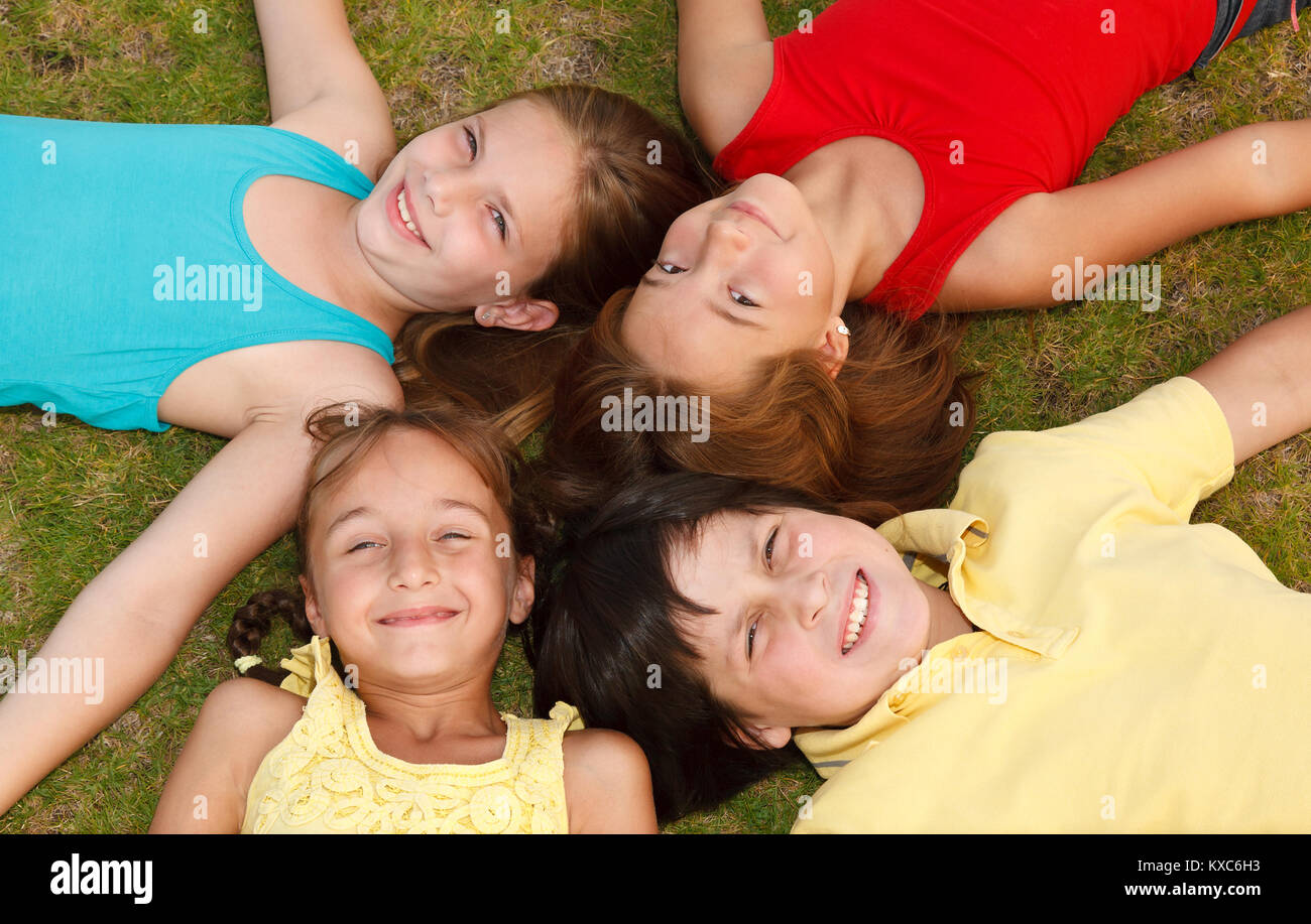 Group of four happy children lying on the grass Stock Photo - Alamy