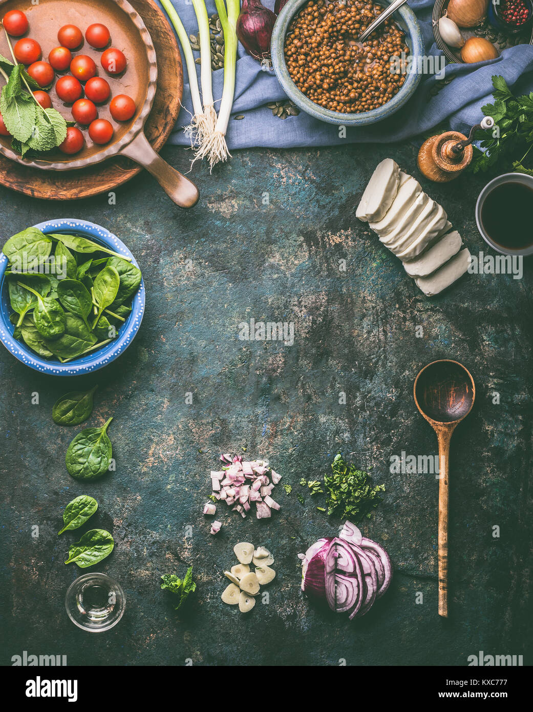 Vegetarian food cooking background. Spinach,tomatoes, lentil and fresh seasoning with cooking spoon on rustic kitchen table background, top view, fram Stock Photo