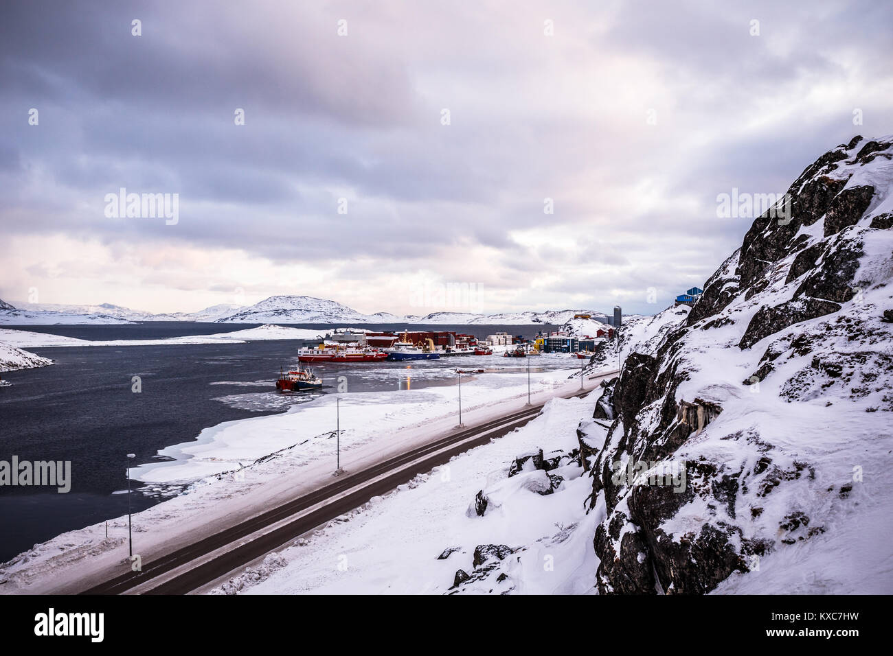 Road to the harbor among the rocks and snow with port of Nuuk in the background, Greenland Stock Photo