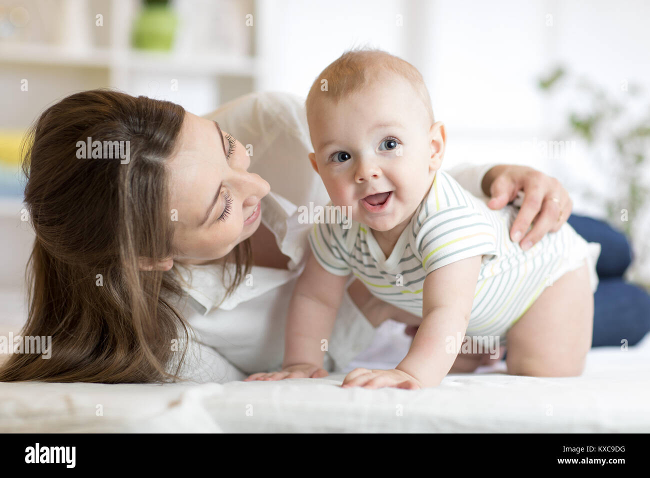 Mom and baby boy playing in sunny bedroom. Parent and little child kid relaxing at home. Family having fun together. Stock Photo