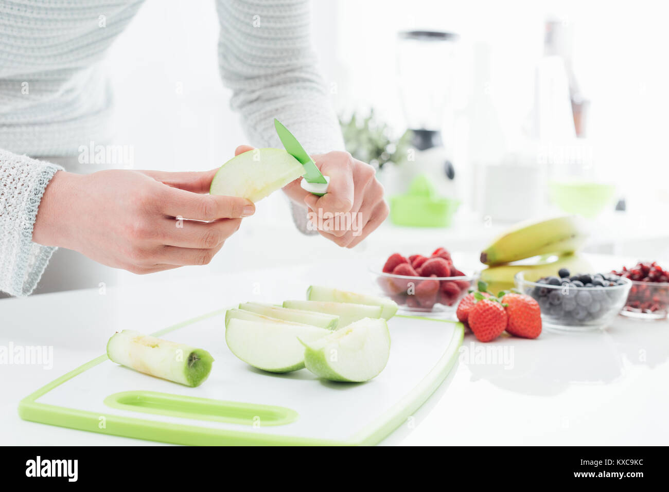 Woman preparing fruit in her kitchen, she is slicing and peeling apples on a chopping board Stock Photo