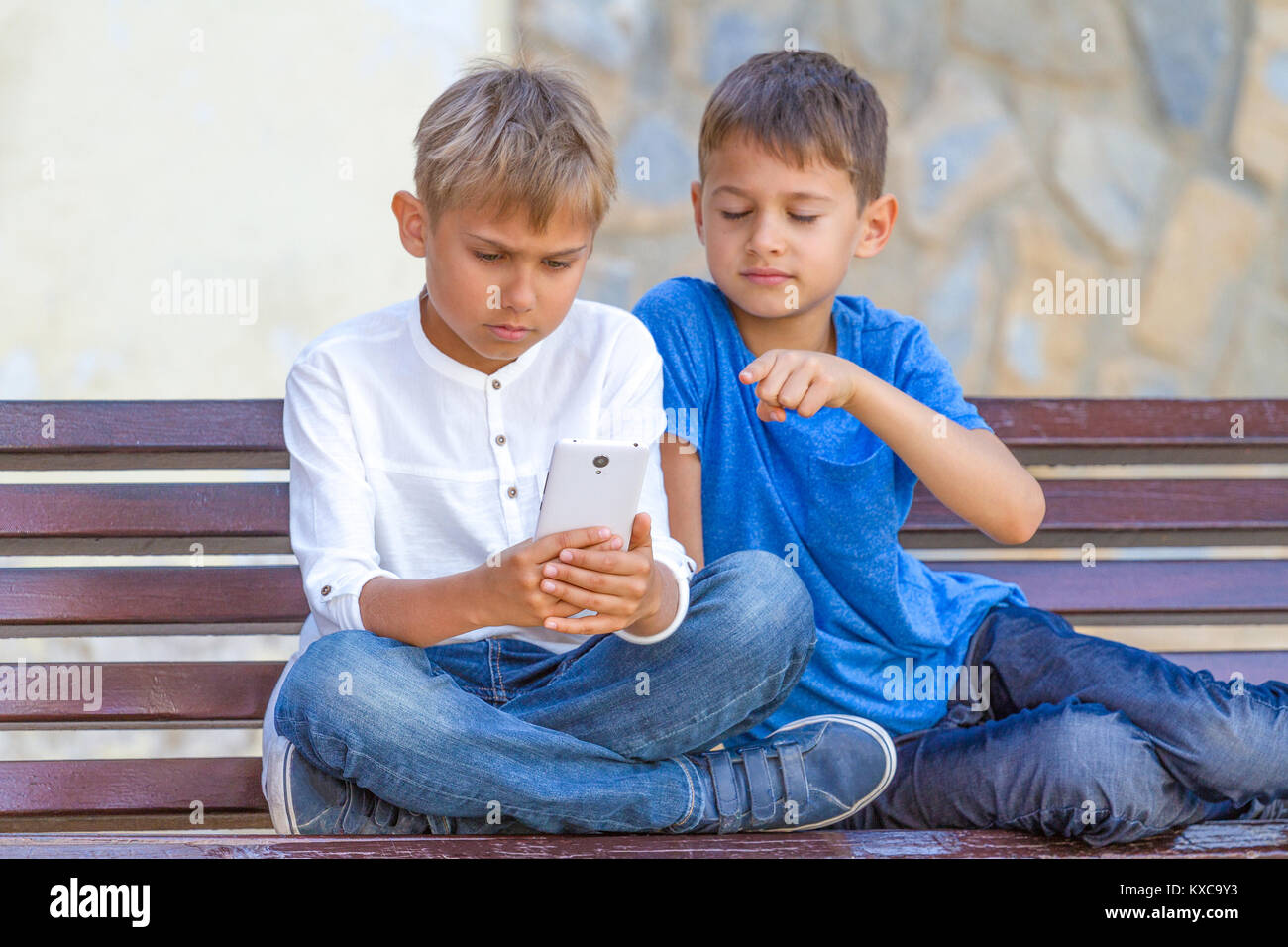 Boys With Mobile Phone Sitting On The Bench Outdoors Stock Photo