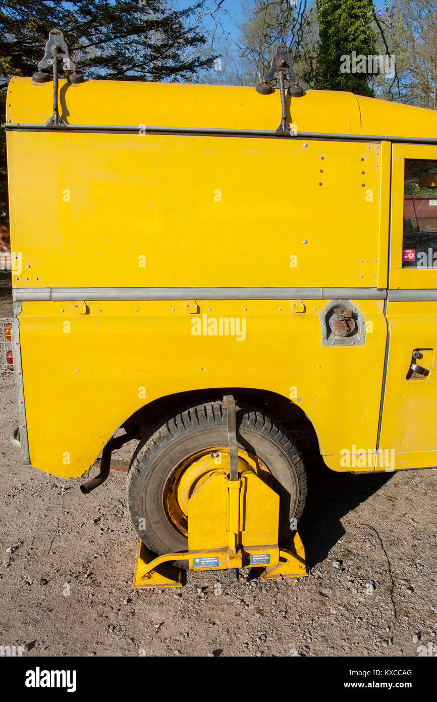 A yellow wheel clamp on a yellow Land Rover Series 3. Parked on private