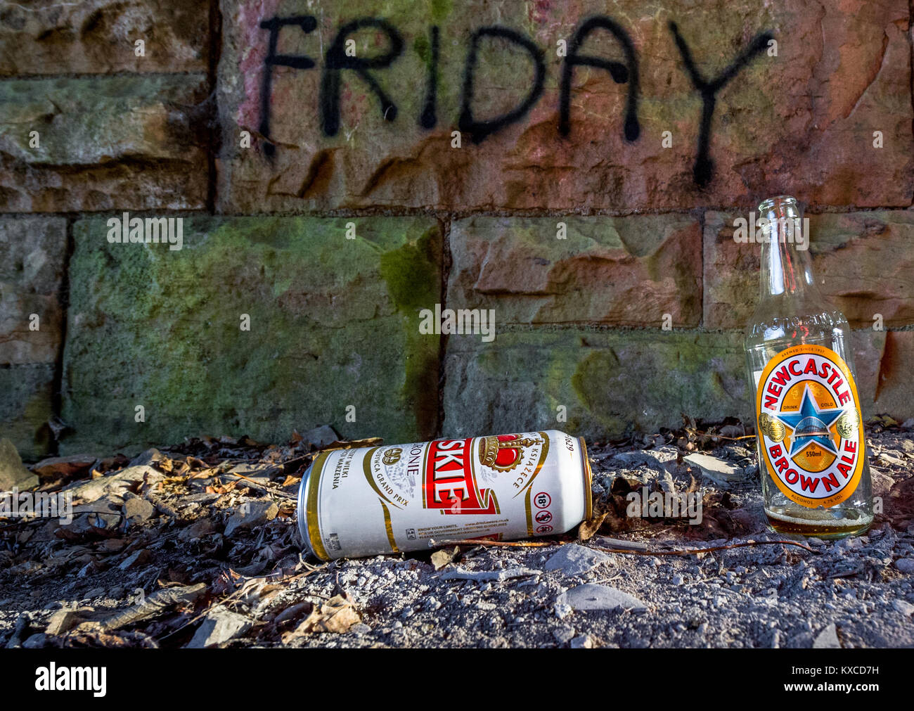 Empty and discarded beer bottle and can against a stone wall with Bad Friday sprayed onto it. Stock Photo