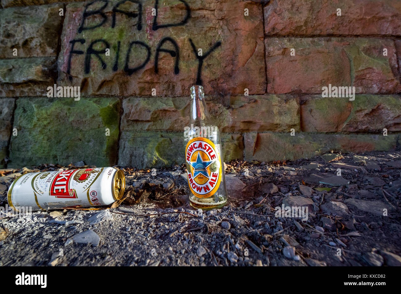 Empty and discarded beer bottle and can against a stone wall with Bad Friday sprayed onto it. Stock Photo