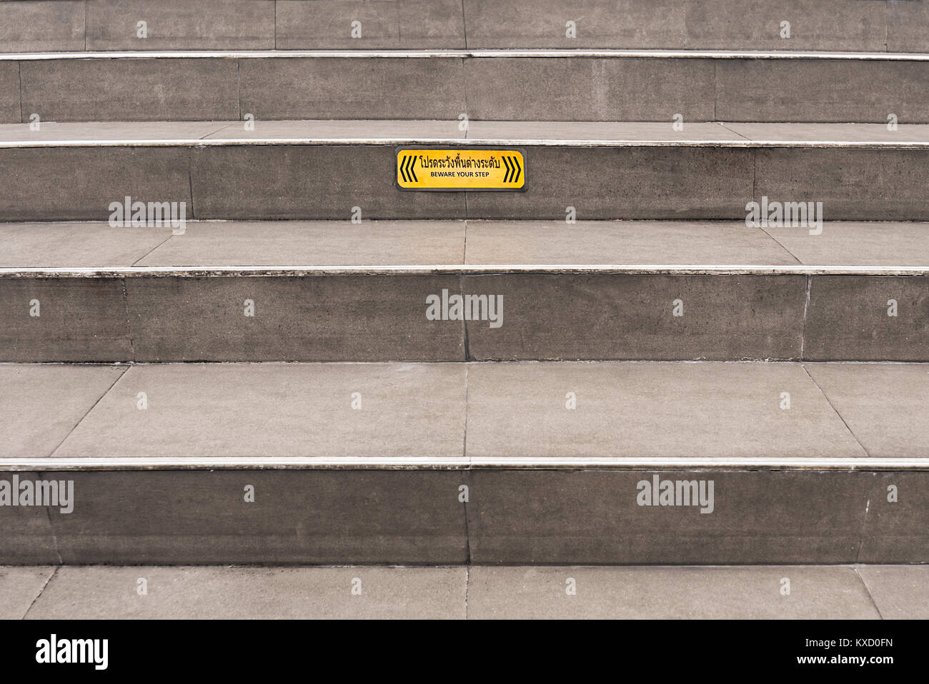 Paved grey public steps with a yellow 'Beware your step' caution sign. Stock Photo