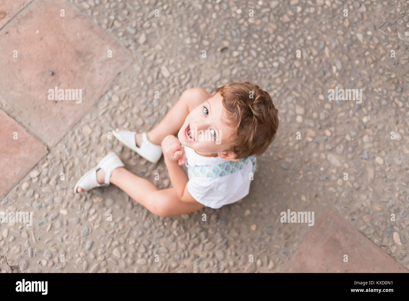 Color photograph, in overhead shot, of a boy sitting on the floor looking towards the camera and smiling. Stock Photo