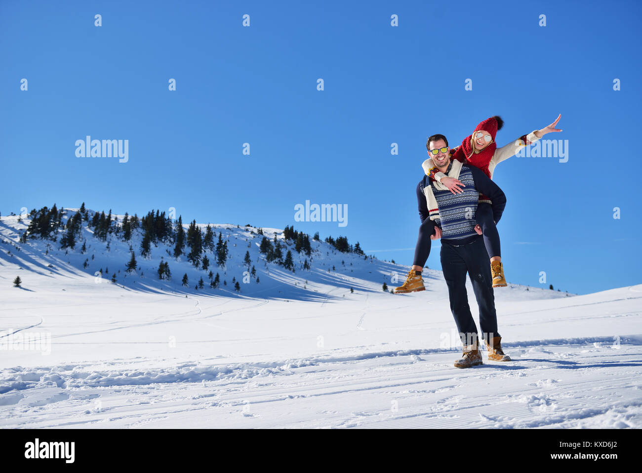 Young couple having fun on snow. Happy man at the mountain giving piggyback ride to his smiling girlfriend. Stock Photo