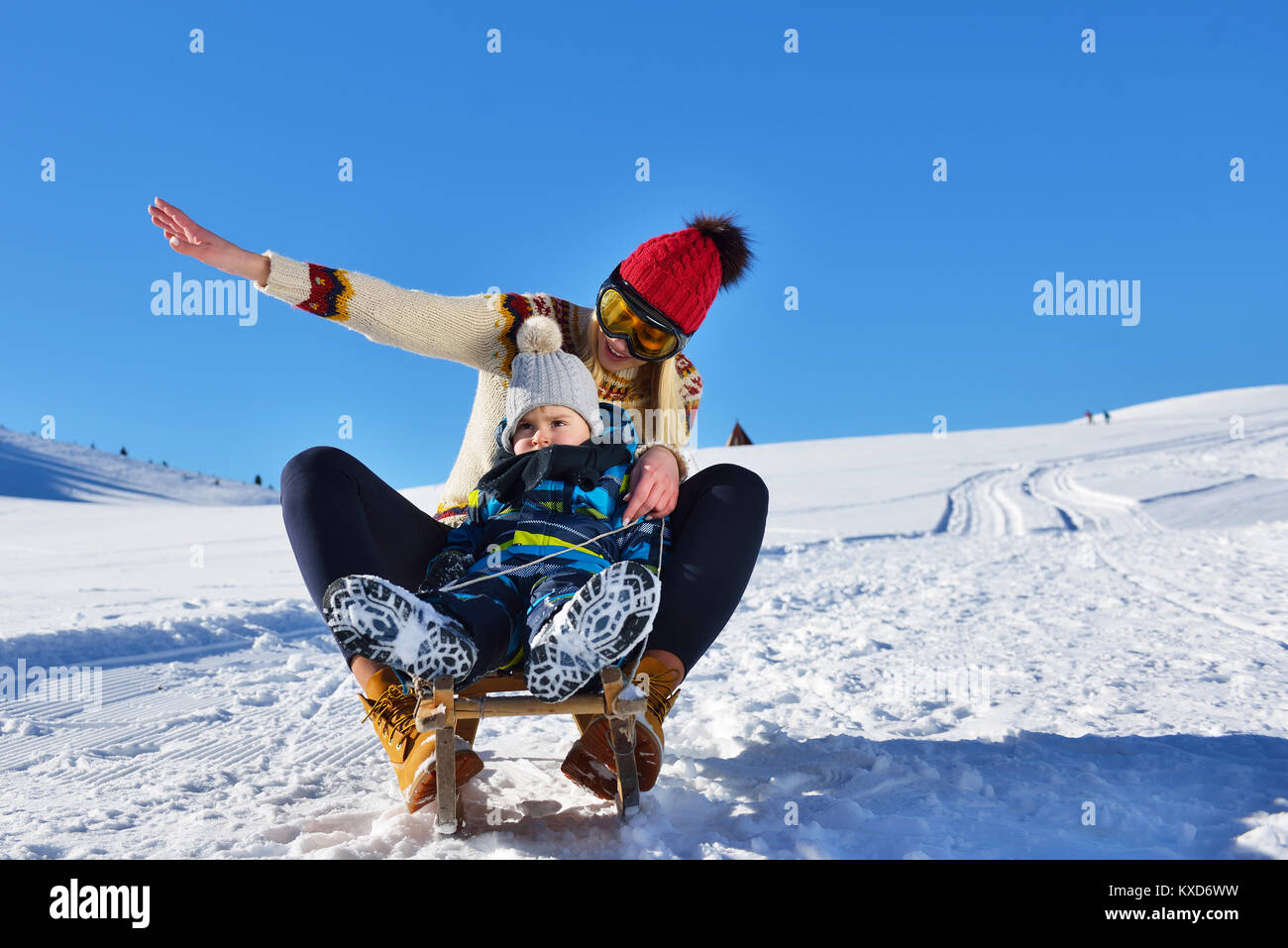 photo of happy mother and child playing in the snow with a sledge in a sunny winter day Stock Photo