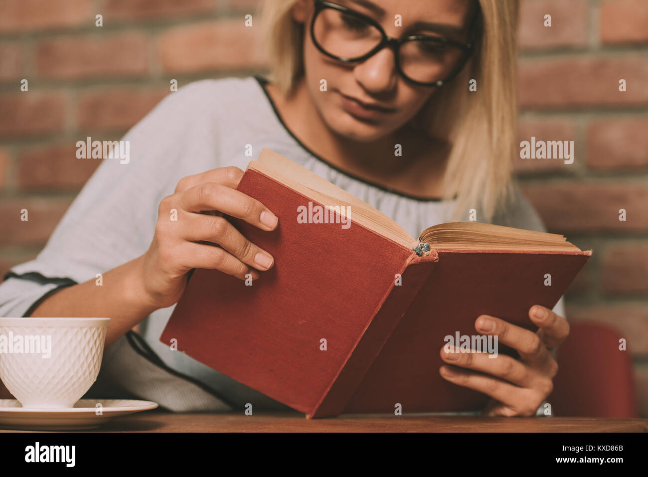 Woman sitting at a table reading a book Stock Photo